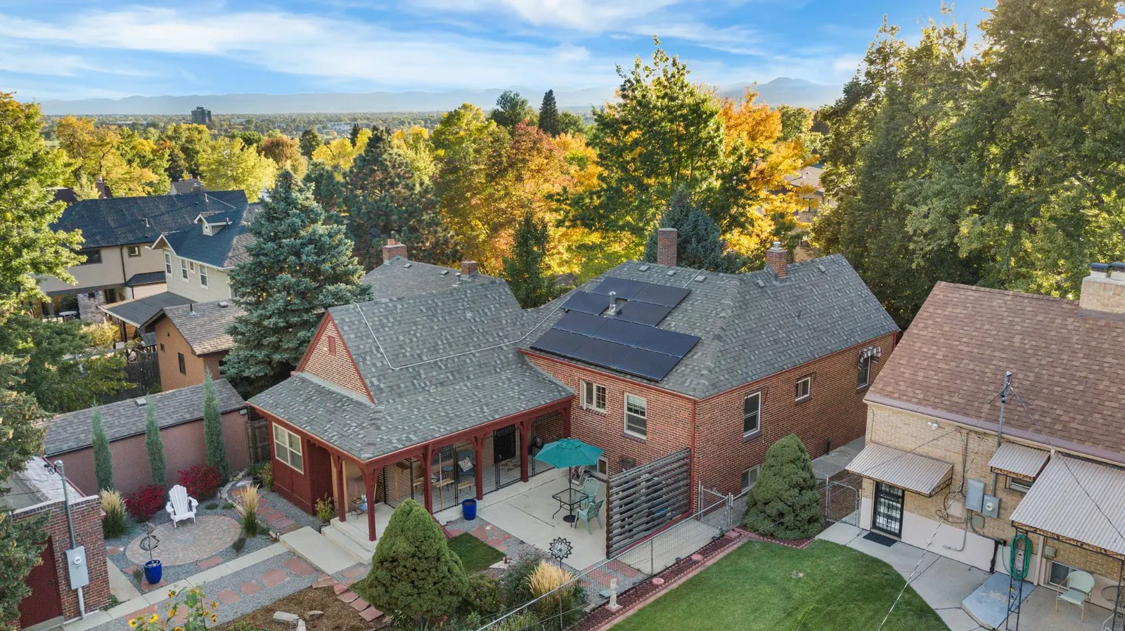 Aerial view of the brick Tudor at 2814 Stuart Street with its solar roof, covered porch and patio, autumn trees and the Front Range beyond