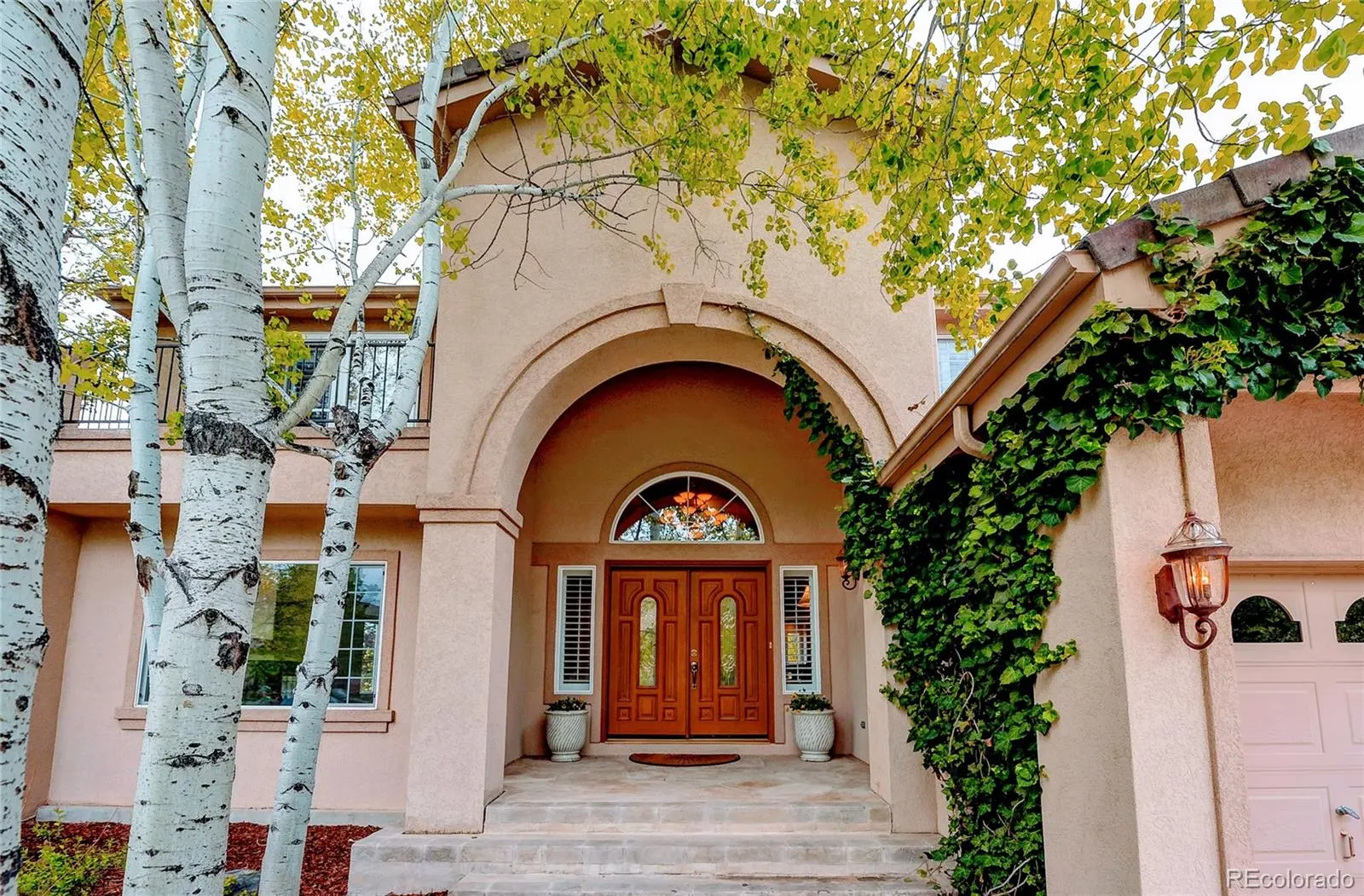 Arched front entry framed by ivy and aspens